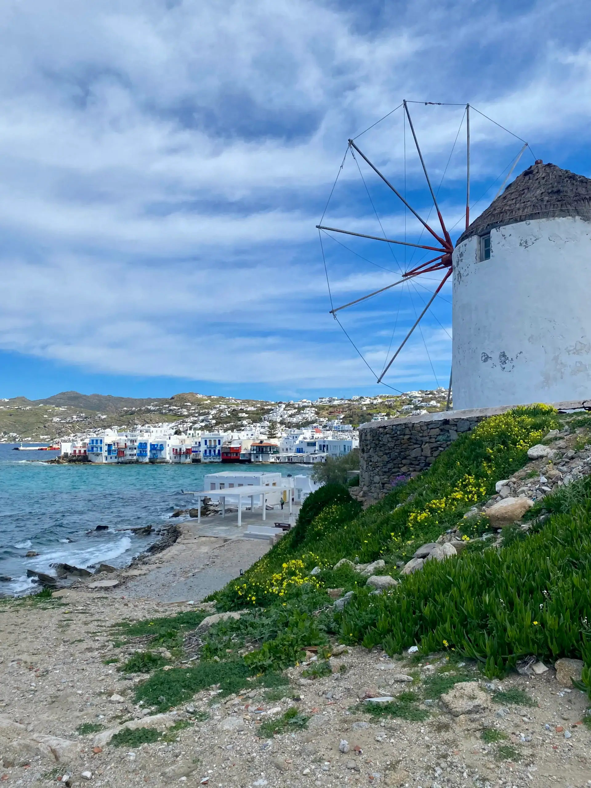 Iconic Greek windmill overlooking the Aegean Sea with white buildings in the background in Mykonos.